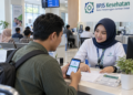 Ilustrasi petugas pelayanan membantu peserta memeriksa status kepesertaan BPJS Kesehatan melalui ponsel di loket