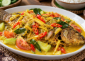 Ikan nila goreng dengan saus bumbu kuning, irisan cabai merah, tomat, dan mentimun pada piring putih