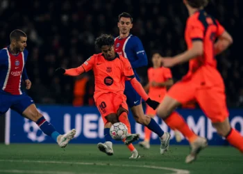 Pemain Barcelona berseragam oranye menendang bola saat dikelilingi pemain Paris Saint-Germain berseragam biru dalam pertandingan sepak bola.