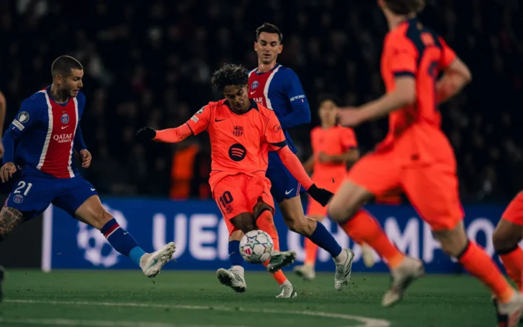 Pemain Barcelona berseragam oranye menendang bola saat dikelilingi pemain Paris Saint-Germain berseragam biru dalam pertandingan sepak bola.