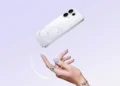Ponsel OPPO berwarna putih terlihat dari sisi belakang dengan tiga kamera, ditampilkan di atas latar ungu muda dan tangan di bawahnya