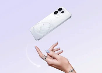 Ponsel OPPO berwarna putih terlihat dari sisi belakang dengan tiga kamera, ditampilkan di atas latar ungu muda dan tangan di bawahnya