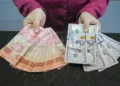 Tangan memegang selembar kumpulan uang rupiah pecahan Rp. 100.000 dan beberapa lembar uang dolar Amerika Serikat pecahan 100 dolar
