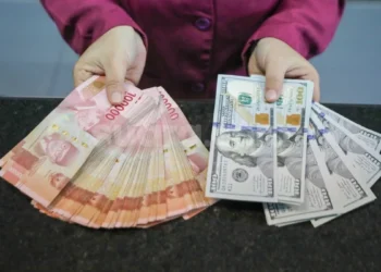 Tangan memegang selembar kumpulan uang rupiah pecahan Rp. 100.000 dan beberapa lembar uang dolar Amerika Serikat pecahan 100 dolar