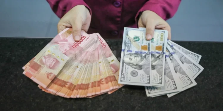 Tangan memegang selembar kumpulan uang rupiah pecahan Rp. 100.000 dan beberapa lembar uang dolar Amerika Serikat pecahan 100 dolar