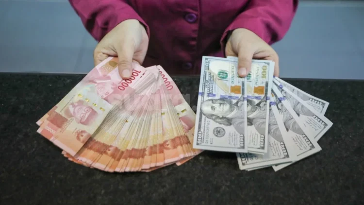 Tangan memegang selembar kumpulan uang rupiah pecahan Rp. 100.000 dan beberapa lembar uang dolar Amerika Serikat pecahan 100 dolar