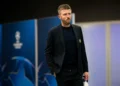 Michael Carrick mengenakan jas hitam dan kaus gelap berjalan di sebuah area stadion.