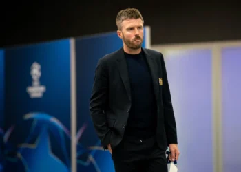 Michael Carrick mengenakan jas hitam dan kaus gelap berjalan di sebuah area stadion.