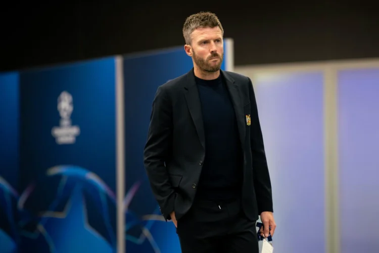 Michael Carrick mengenakan jas hitam dan kaus gelap berjalan di sebuah area stadion.