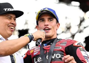 Marc Marquez mengenakan pakaian balap Ducati dan topi, berbicara di depan mikrofon saat diwawancarai