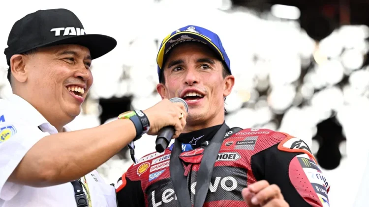 Marc Marquez mengenakan pakaian balap Ducati dan topi, berbicara di depan mikrofon saat diwawancarai