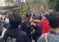Sejumlah aparat kepolisian berhelm dan mengenakan perlengkapan pengamanan berada di antara warga di sebuah jalan permukiman