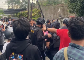 Sejumlah aparat kepolisian berhelm dan mengenakan perlengkapan pengamanan berada di antara warga di sebuah jalan permukiman
