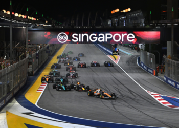 Sejumlah mobil Formula 1 melaju di lintasan Marina Bay pada malam hari di bawah papan bertuliskan Singapore