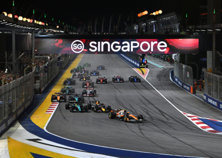 Sejumlah mobil Formula 1 melaju di lintasan Marina Bay pada malam hari di bawah papan bertuliskan Singapore