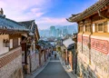 Jalan di antara rumah-rumah hanok tradisional beratap genteng di Bukchon, Seoul, dengan gedung-gedung kota di kejauhan