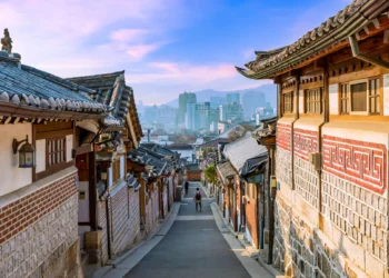 Jalan di antara rumah-rumah hanok tradisional beratap genteng di Bukchon, Seoul, dengan gedung-gedung kota di kejauhan