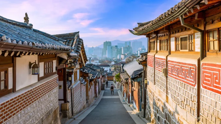 Jalan di antara rumah-rumah hanok tradisional beratap genteng di Bukchon, Seoul, dengan gedung-gedung kota di kejauhan