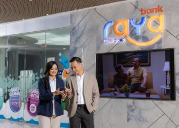 Dua orang melihat layar ponsel di depan logo Bank Raya