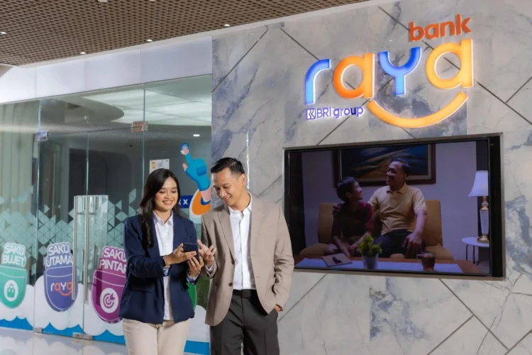 Dua orang melihat layar ponsel di depan logo Bank Raya