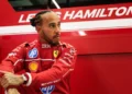 Lewis Hamilton mengenakan seragam balap merah Ferrari di depan panel bertuliskan namanya