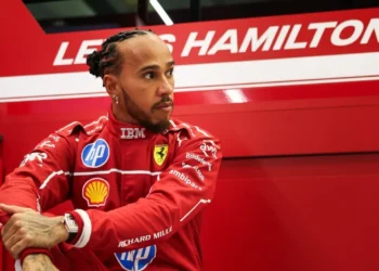 Lewis Hamilton mengenakan seragam balap merah Ferrari di depan panel bertuliskan namanya