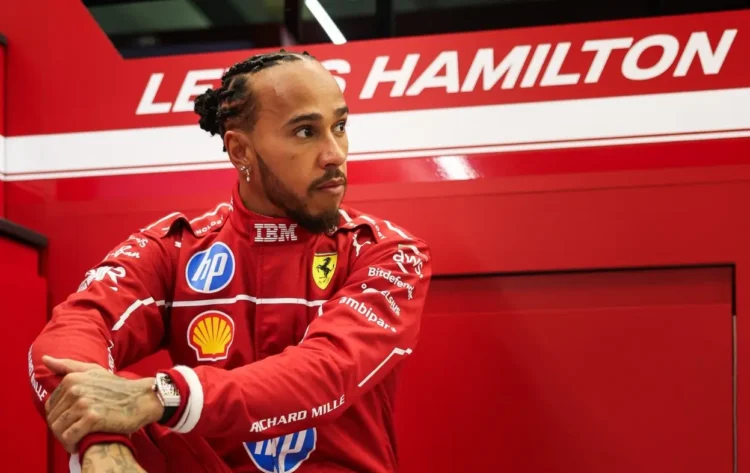 Lewis Hamilton mengenakan seragam balap merah Ferrari di depan panel bertuliskan namanya