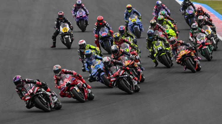 Sejumlah pembalap MotoGP melaju berkelompok melewati tikungan lintasan balap.