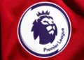 Logo Premier League bergambar kepala singa bermahkota pada permukaan kain merah.
