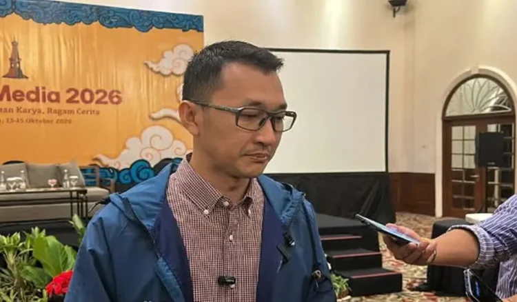 Seorang pria berkacamata mengenakan jaket biru sedang diwawancarai oleh wartawan di dalam ruangan