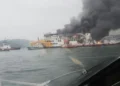 Kapal feri di perairan mengeluarkan asap hitam tebal, dengan beberapa kapal kecil berada di dekatnya