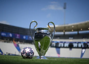 Trofi Liga Champions UEFA berdiri di lapangan sepak bola dengan bola bermotif bintang di sampingnya