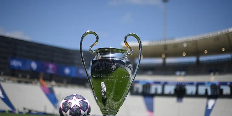 Trofi Liga Champions UEFA berdiri di lapangan sepak bola dengan bola bermotif bintang di sampingnya