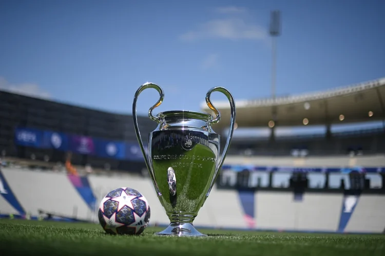 Trofi Liga Champions UEFA berdiri di lapangan sepak bola dengan bola bermotif bintang di sampingnya