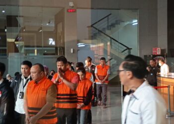 Sejumlah orang mengenakan rompi tahanan oranye dikawal petugas di dalam gedung