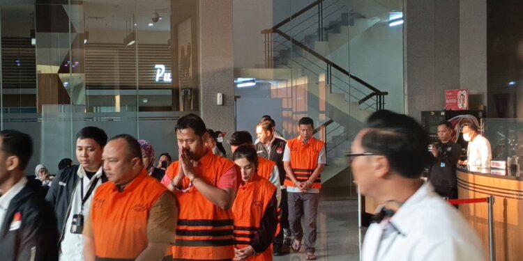 Sejumlah orang mengenakan rompi tahanan oranye dikawal petugas di dalam gedung