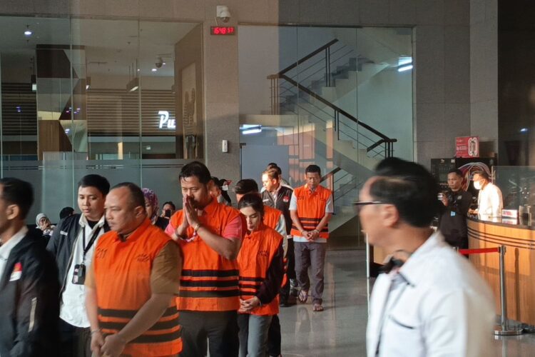 Sejumlah orang mengenakan rompi tahanan oranye dikawal petugas di dalam gedung