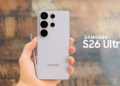 Bagian belakang Samsung Galaxy S26 Ultra berwarna abu-abu terang dipegang dengan tangan, terlihat kamera belakang dan S Pen, disertai tulisan Samsung S26 Ultra