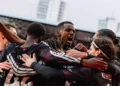 Sejumlah pemain Liverpool mengenakan seragam gelap saling merangkul di lapangan.