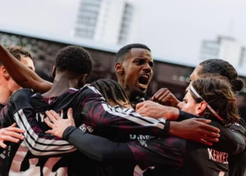 Sejumlah pemain Liverpool mengenakan seragam gelap saling merangkul di lapangan.
