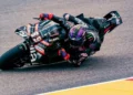 Pembalap mengendarai motor balap Aprilia berwarna gelap saat menikung di lintasan