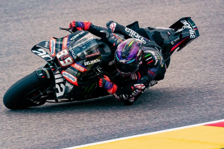 Pembalap mengendarai motor balap Aprilia berwarna gelap saat menikung di lintasan