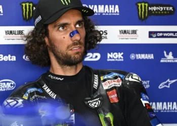 Alex Rins mengenakan baju balap Monster Energy Yamaha dan topi hitam di depan latar sponsor Yamaha