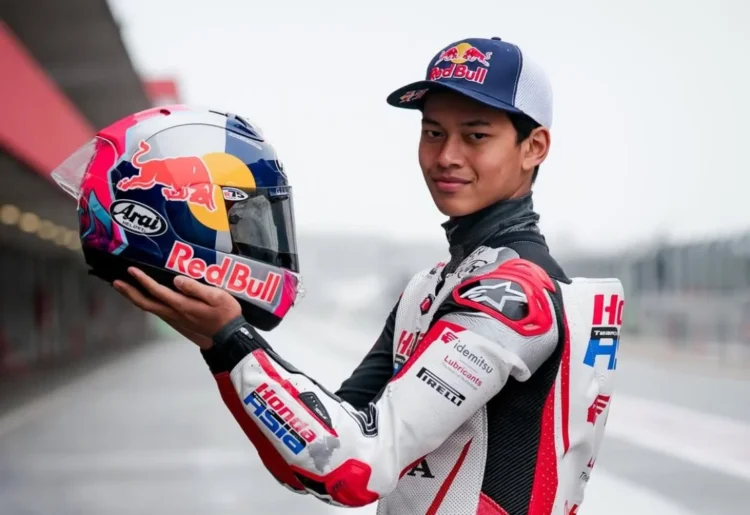 Veda Ega Pratama mengenakan baju balap Honda Team Asia sambil memegang helm berlogo Red Bull