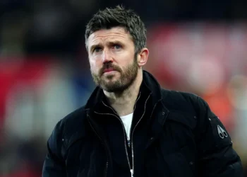 Michael Carrick mengenakan jaket hitam dengan latar tribun stadion yang tidak fokus