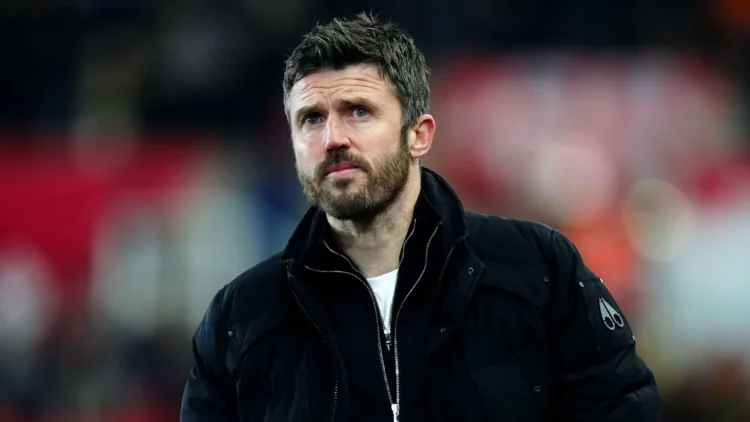 Michael Carrick mengenakan jaket hitam dengan latar tribun stadion yang tidak fokus