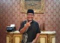 Denny Indrayana berdiri di dalam ruangan mengenakan peci hitam