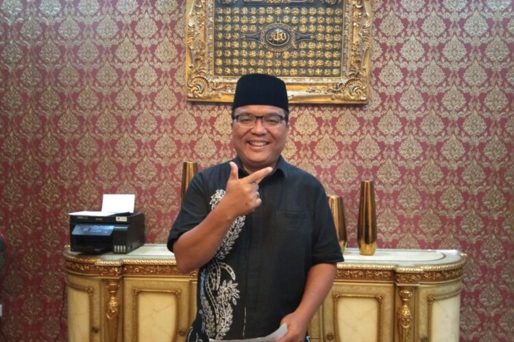 Denny Indrayana berdiri di dalam ruangan mengenakan peci hitam