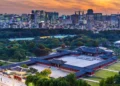 Pemandangan bangunan istana tradisional Korea dengan taman hijau dan gedung-gedung modern di belakangnya saat matahari terbenam