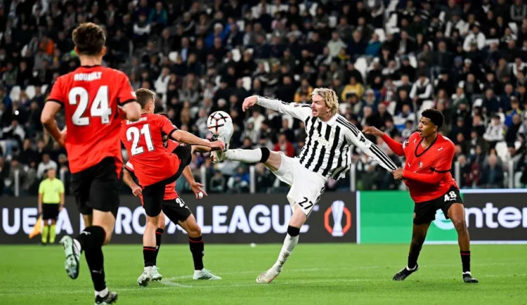 Pemain Juventus berseragam hitam putih berusaha menjangkau bola di antara pemain Rennes berseragam merah di lapangan.